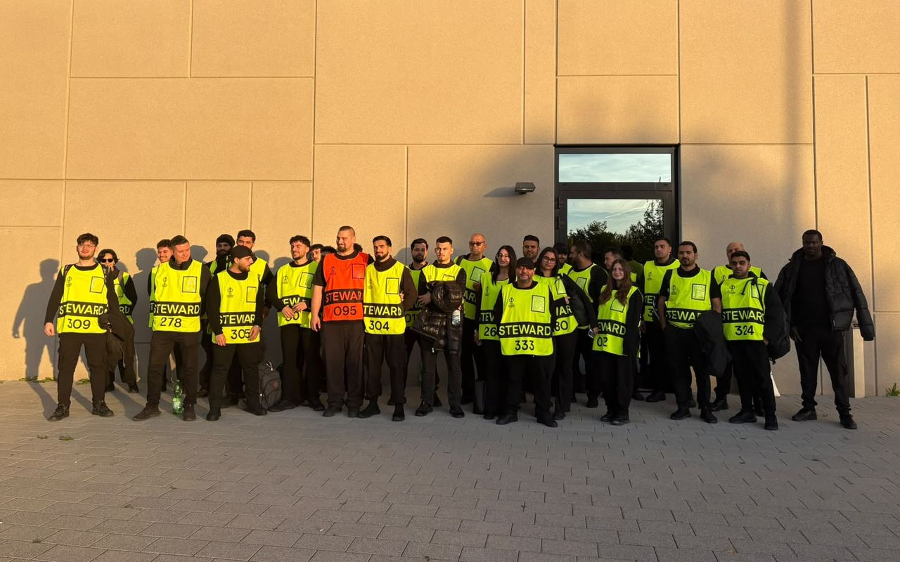 Gruppe von Mitarbeitenden in gelben Steward Westen vor einer hellen Gebäudewand
